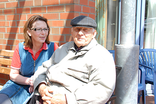 Bewohner und Pfleger sitzen draußen zusammen auf einer Bank