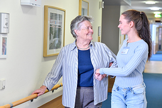 Pflegerin begleitet Bewohnerin durch den Flur 