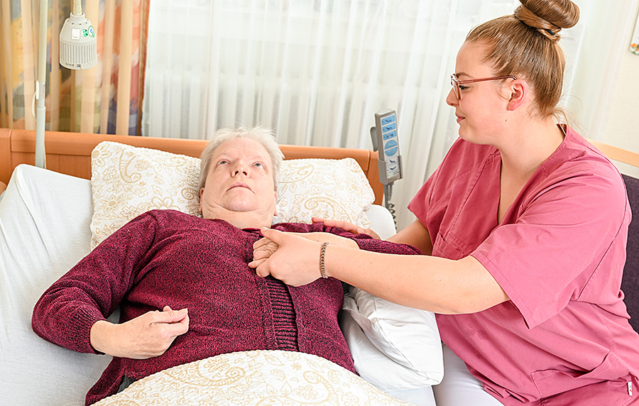 Patientin in Wachkoma Pflegeeinrichtung der Malteser, umgeben von einer einfühlsamen Pflegekraft.