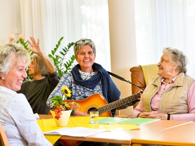 die Tagespflege spielt den Bewohner ein Lied mit einer Gitarre vor 