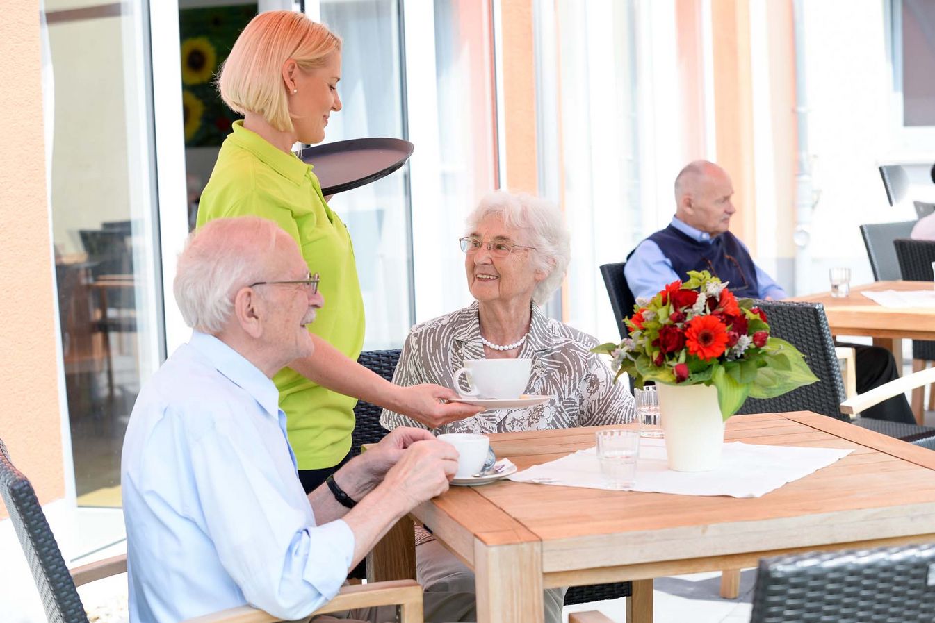 Pflegerin serviert den Bewohnern einen Kaffee auf die Terrasse  