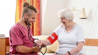 Pfleger misst einer älteren Frau in ihrem Zimmer den Blutdruck.